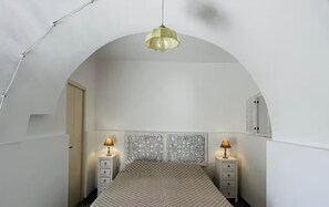 Un dormitorio con cama, dos mesitas de noche, lámpara colgante y cabecero decorativo.