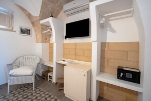Ein Zimmer mit einem weißen Korbstuhl, einem kleinen Schrank, einem an der Wand befestigten Fernseher und einem fest montierten Safe.