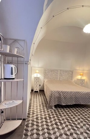Un dormitorio con suelo de cuadros, una cama con cabecero estampado, una estantería con una tetera y dos lámparas de noche.