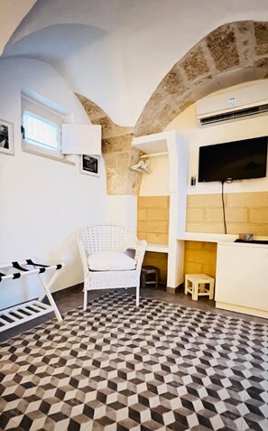 Una habitación con piso a cuadros, una silla blanca, una mesita, un televisor y una chimenea.