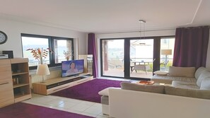A modern living room with a television, a sofa, a coffee table, and a view of the outside.