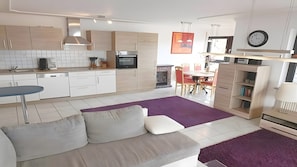 A modern kitchen with white cabinets, a built-in oven, and a dining area with a table and chairs.