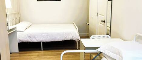 Una habitación pequeña y limpia con dos camas, una mesita de noche, una silla y un cuadro en la pared.
