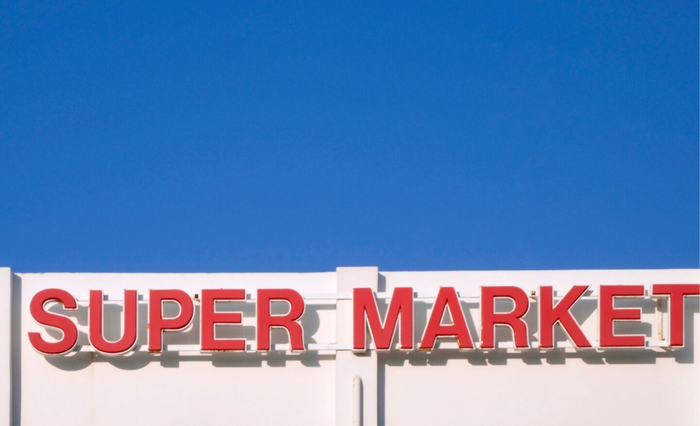 Un letrero con la inscripción 'SUPER MARKET' en letras rojas grandes sobre un fondo blanco.