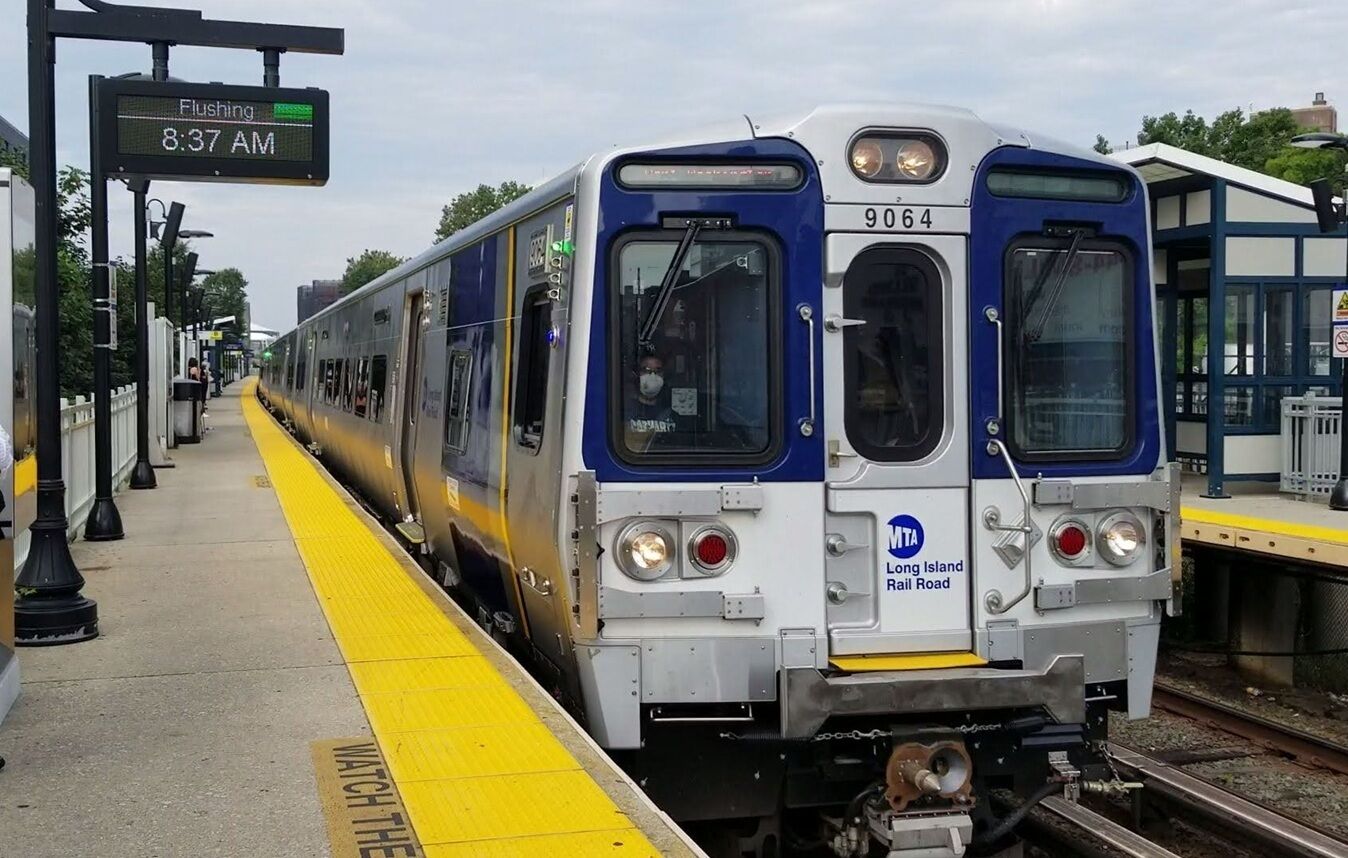 A train at a station platform with a sign indicating 'Flushing 8:37 AM'.