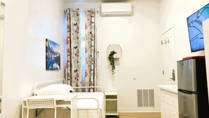 Una habitación pequeña y limpia con cama, escritorio, refrigerador y televisor de pared.