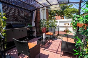 A patio with a brick wall, a grill, wicker furniture, and potted plants.