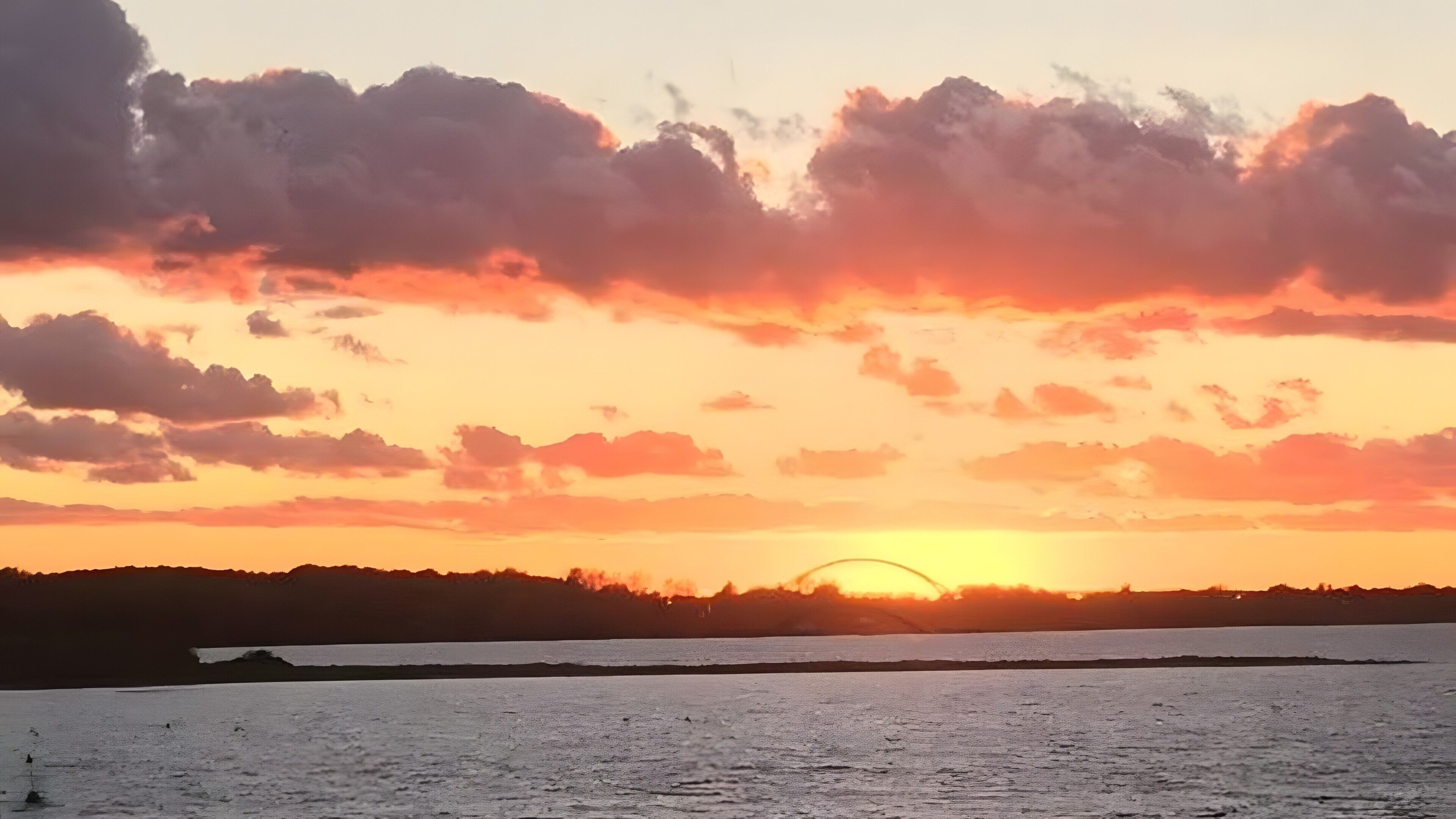 A sunset over a body of water with clouds in the sky.