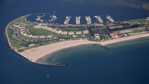 An aerial view of a coastal area with a marina, beachfront, and residential buildings.