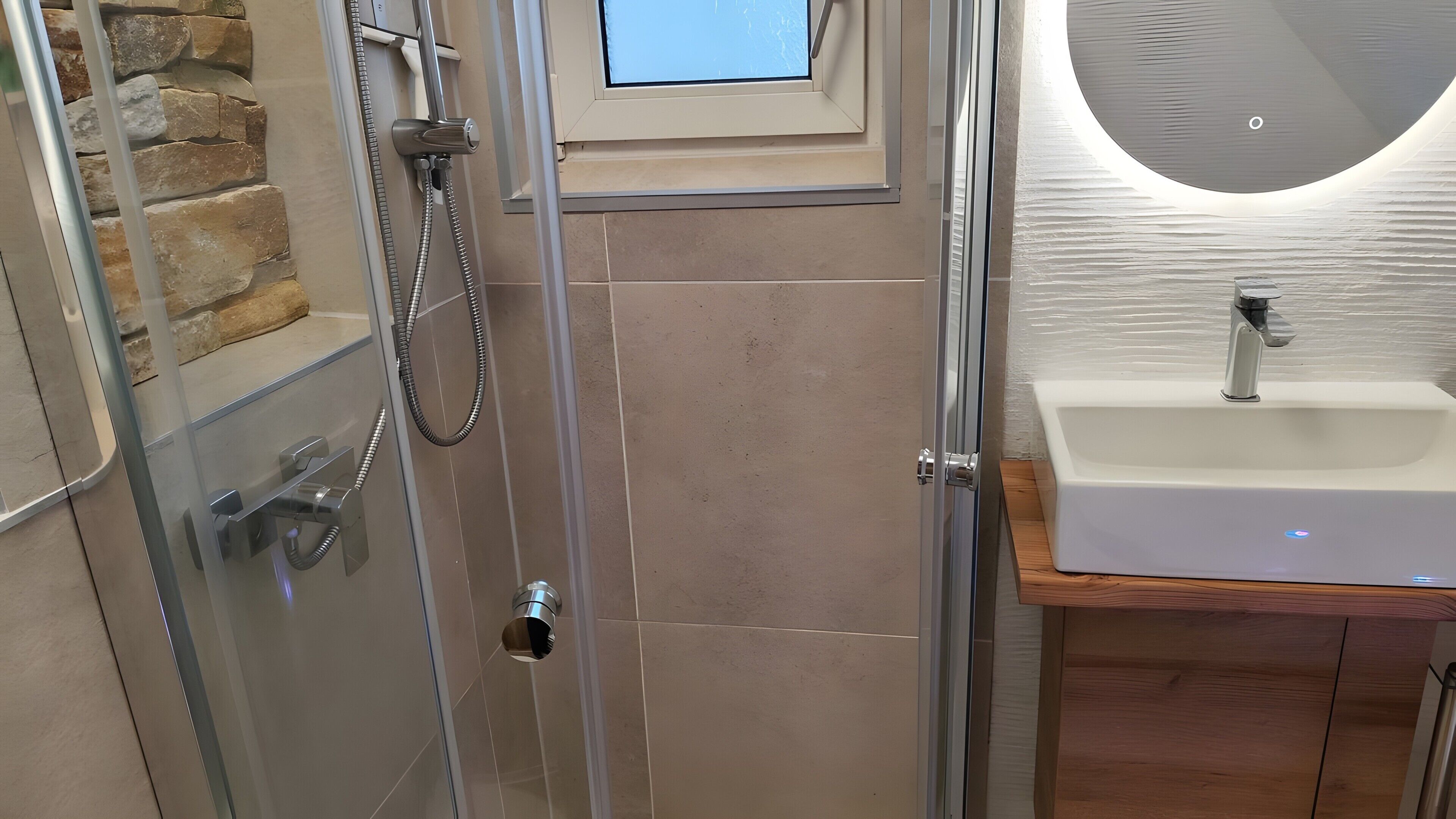 Ein Badezimmer mit einer gläsernen Duschkabine, einem weißen Waschbecken und einer Steinwand.