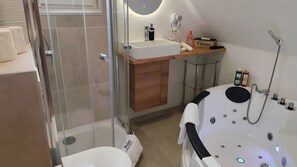 A modern bathroom with a glass shower enclosure, a white bathtub with multiple controls, a wooden vanity with a sink, and a towel rack. - Apartment in Daun for up to 8 Guests (95 m²) – Central Location (Daun)
