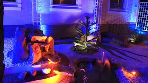 Un jardín exterior con un brasero, rocas y un árbol pequeño.