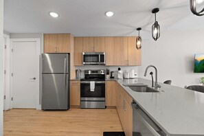 A modern kitchen with stainless steel appliances, wooden cabinets, a large island with a sink, and recessed ceiling lighting. - Upscale 2BD | Sleeps 4 | Historic Center City Apt (Philadelphia)