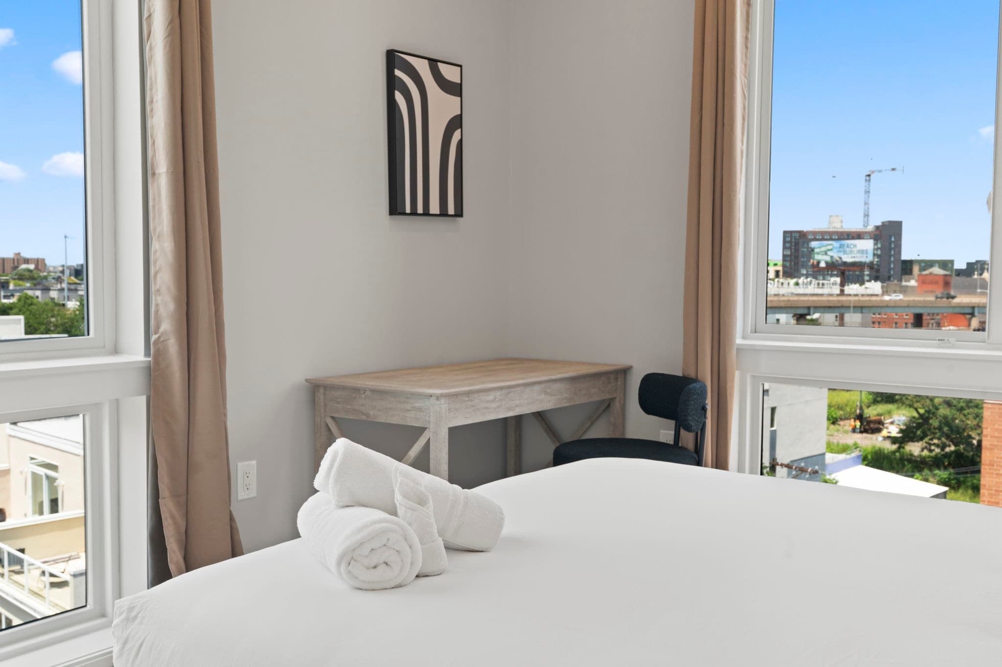 A hotel room with a bed, a small table, a chair, a window with curtains, and a city view.