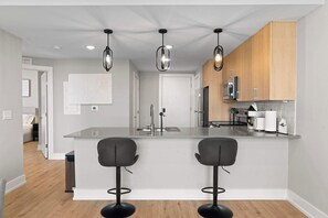 Una cocina moderna con una isla central, taburetes de bar, lámparas colgantes y armarios de madera.