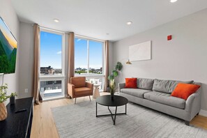 A modern living room with a sofa, armchair, and coffee table, large windows with a view, and a painting on the wall. - Upscale 2BD | Sleeps 4 | Historic Center City Apt (Philadelphia)