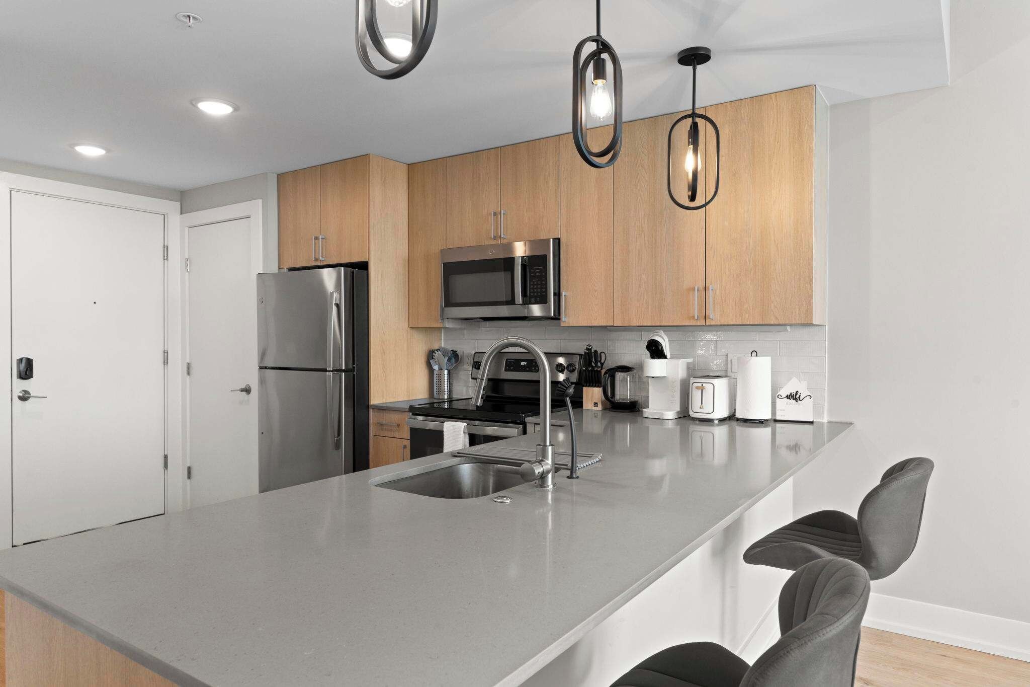 A modern kitchen with stainless steel appliances, a central island with seating, and pendant lighting.