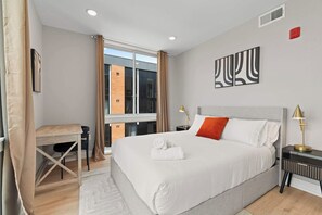 A hotel room with a bed, a desk, a chair, a window, and artwork on the wall. - Upscale 2BD | Sleeps 4 | Historic Center City Apt (Philadelphia)