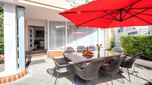 En udendørs patio med et bord, stole og en rød parasol, samt udsigt over det omkringliggende område.