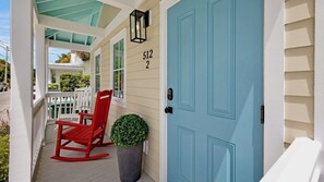 Eine Veranda mit einem roten Schaukelstuhl, einem Blumentopf und einer blauen Tür mit der Nummer 512.