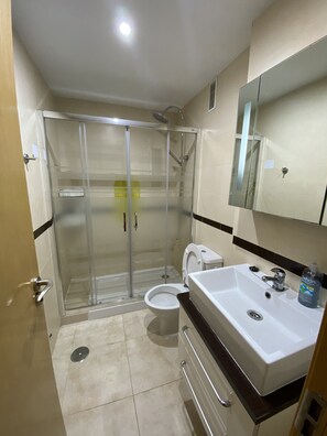 Ein Badezimmer mit einer Duschkabine, einer Toilette, einem Waschbecken mit Spiegel und einer Handseifenflasche.