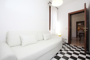 A white sofa with a lamp, a checkered floor, and a doorway leading to another room. - Puccini Historical Center (Venice)
