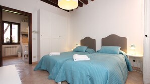 Un dormitori amb dos llits, un armari blanc, una tauleta de nit amb una làmpada i una finestra.