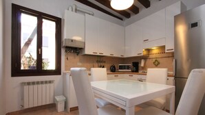Una cuina moderna amb armaris blancs, una taula de vidre i cadires blanques.
