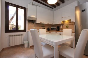 A modern kitchen with white cabinets, a glass-top table, and white chairs. - Puccini Historical Center (Venice)