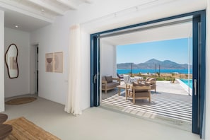 A modern living room with a large sliding glass door leading to a balcony with a pool and a view of the sea. - Villa Nabia I, Seaview and Sunset view, Private Pool (Adamas)