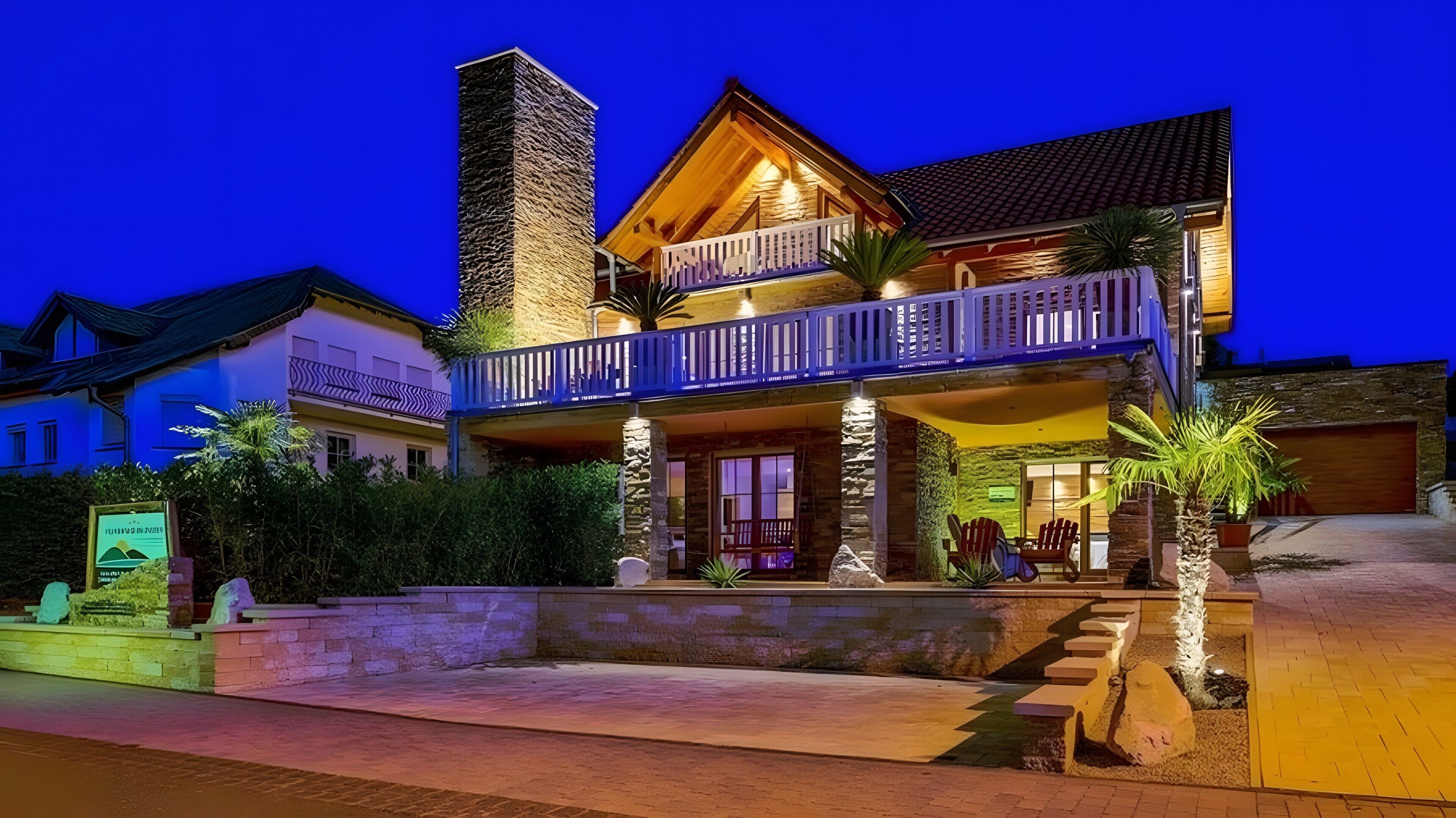 A two-story building with a balcony, stone facade, and a garage.. Luxury Apartment Chalet Near the Lake in Schalkenmehren – Up to 5 Guests (90 m²)