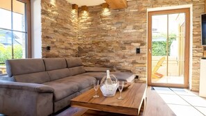 Ein modernes Wohnzimmer mit einer Steinwand, einem braunen Sofa, einem Holztisch und einer GlastĂŒr, die nach drauĂen fĂŒhrt.