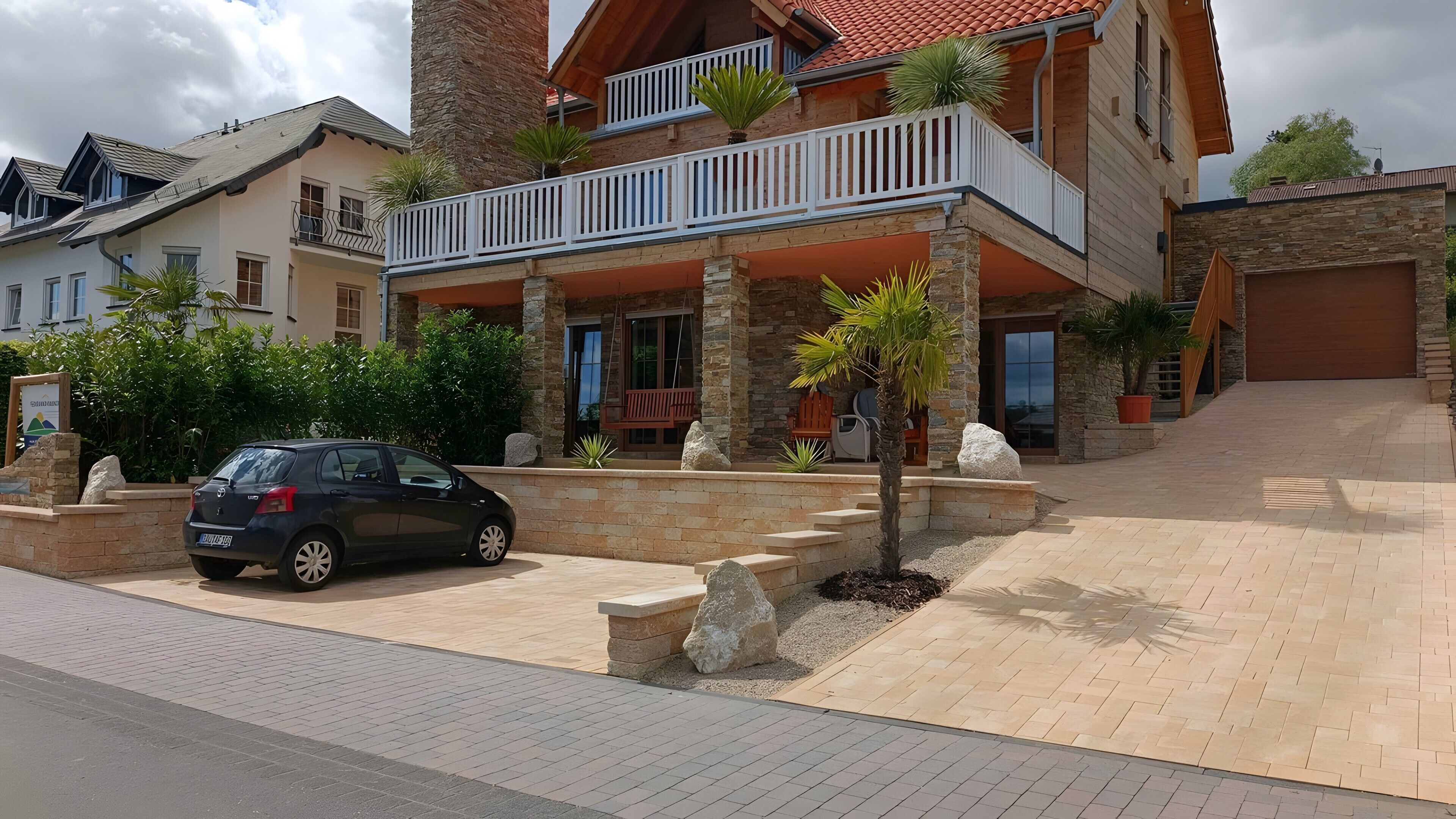 Un edificio residencial de varios pisos con un balcón, pilares de piedra y un coche en la entrada.