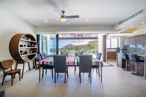 Un comedor moderno con una mesa, sillas, ventilador de techo y vistas al exterior.