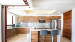 A modern kitchen with wooden cabinets, stainless steel appliances, a built-in microwave, and a central island with bar stools. - Family Paradise Views, Jacuzzi and Beach Club (Cruz de Huanacaxtle)