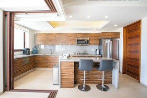 Una cocina moderna con armarios de madera, electrodomésticos de acero inoxidable, un microondas integrado y una isla central con taburetes de bar.