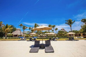 Un resort en la playa con sillones de descanso, sombrillas y edificios de techo de paja.