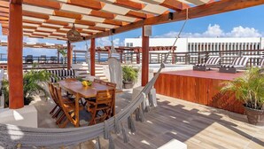 A wooden deck with a table and chairs, a hammock, and a view of the sea. - Private Pool on Luxury PentHouse (Playa del Carmen)