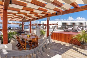 Eine Holzterrasse mit Tisch, Stühlen und einer Hängematte, mit Blick auf das Meer.