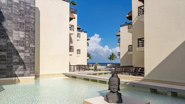 A resort pool with a Buddha statue, clear water, and a view of the ocean. - Private Pool on Luxury PentHouse (Playa del Carmen)