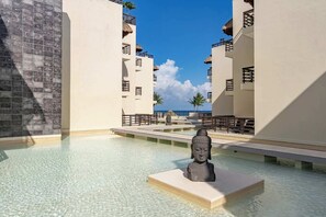 Ein Pool im Resort mit einer Buddha-Statue, klarem Wasser und Blick auf den Ozean.
