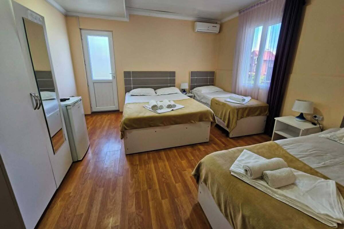 Habitació d'hotel amb dos llits, un escriptori petit, un mirall i una finestra amb cortines.