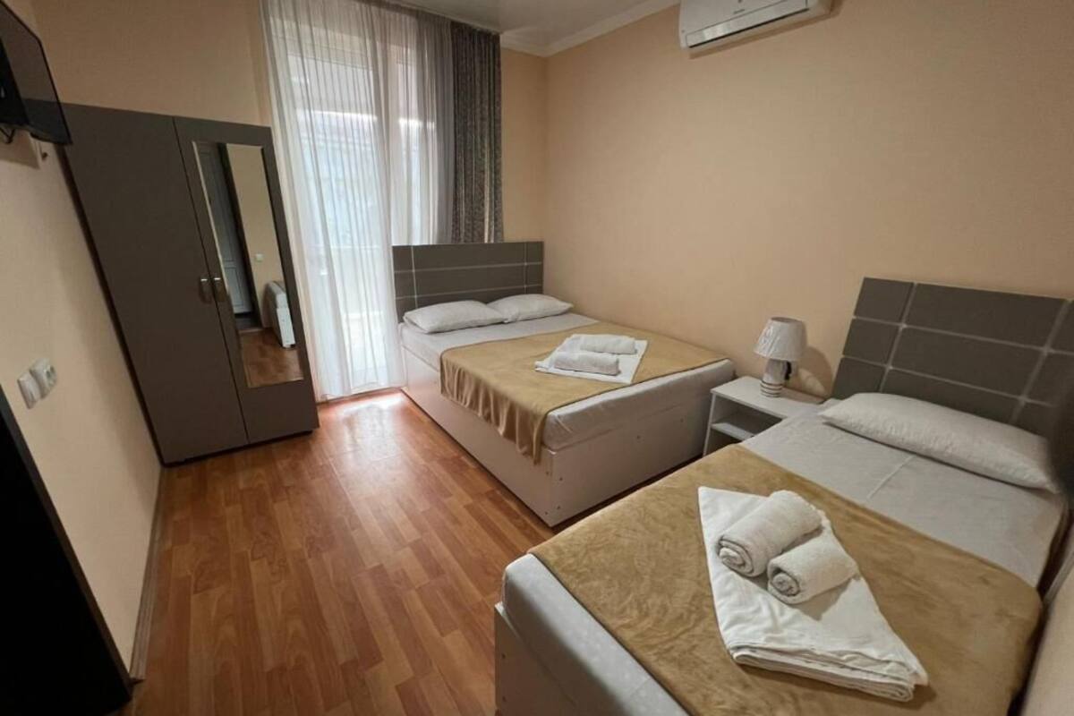 Una habitació d'hotel amb dos llits, un armari, un mirall, una finestra amb cortines i un aparell d'aire condicionat.