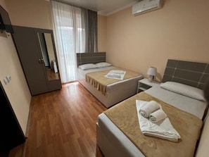 Una habitación de hotel con dos camas, un armario, un espejo, una ventana con cortinas y un equipo de aire acondicionado.