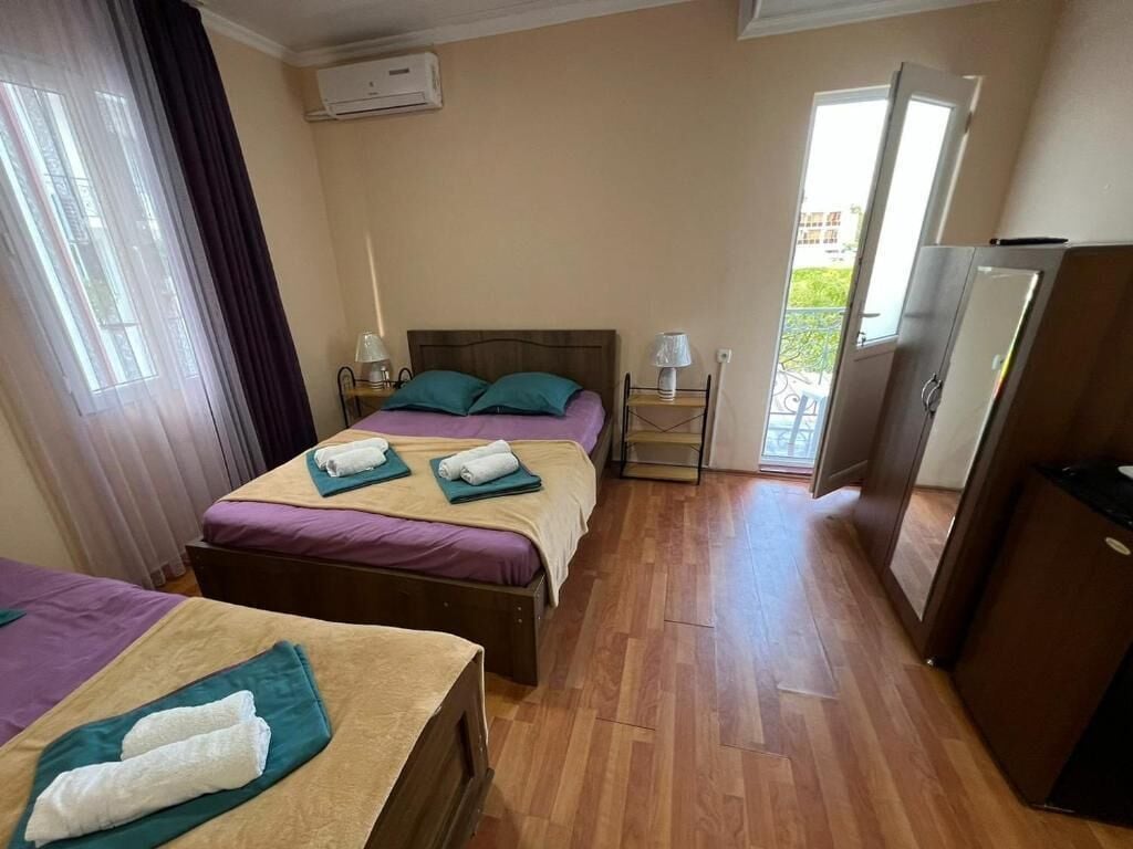 A hotel room with two beds, a wardrobe, a desk, a lamp, and a window with curtains.