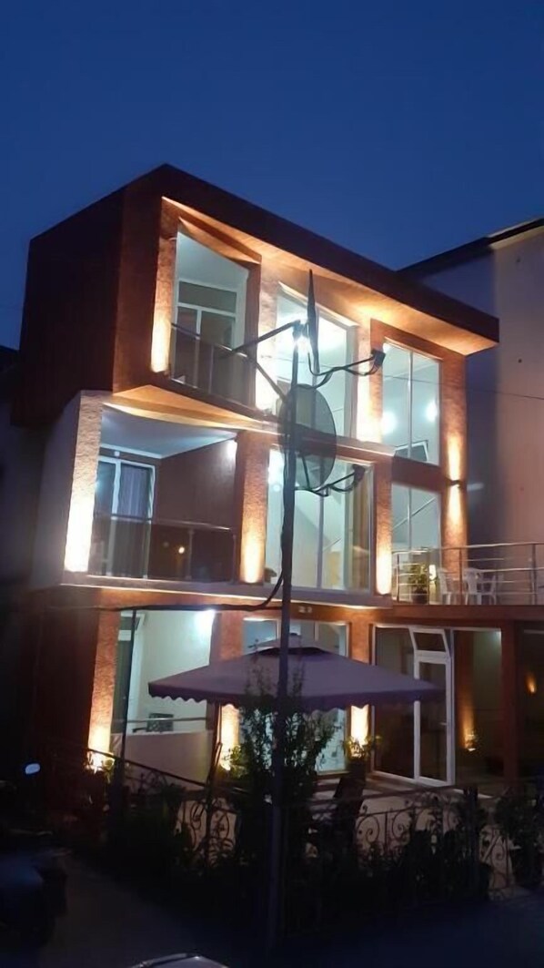A multi-story building with large windows, a balcony, and a patio area with outdoor seating. - hotel IMERI (Ureki)