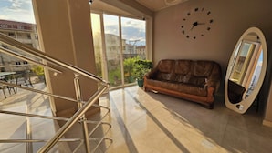 Una habitación amplia con una escalera, un sofá de cuero marrón, un reloj de pared y un ventanal con vistas a edificios.