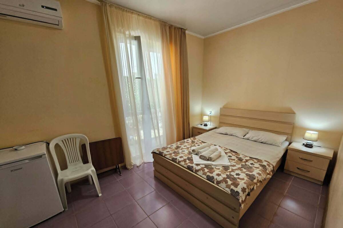 Una habitació d'hotel amb un llit, un escriptori, una cadira i una tauleta de nit amb una làmpada.