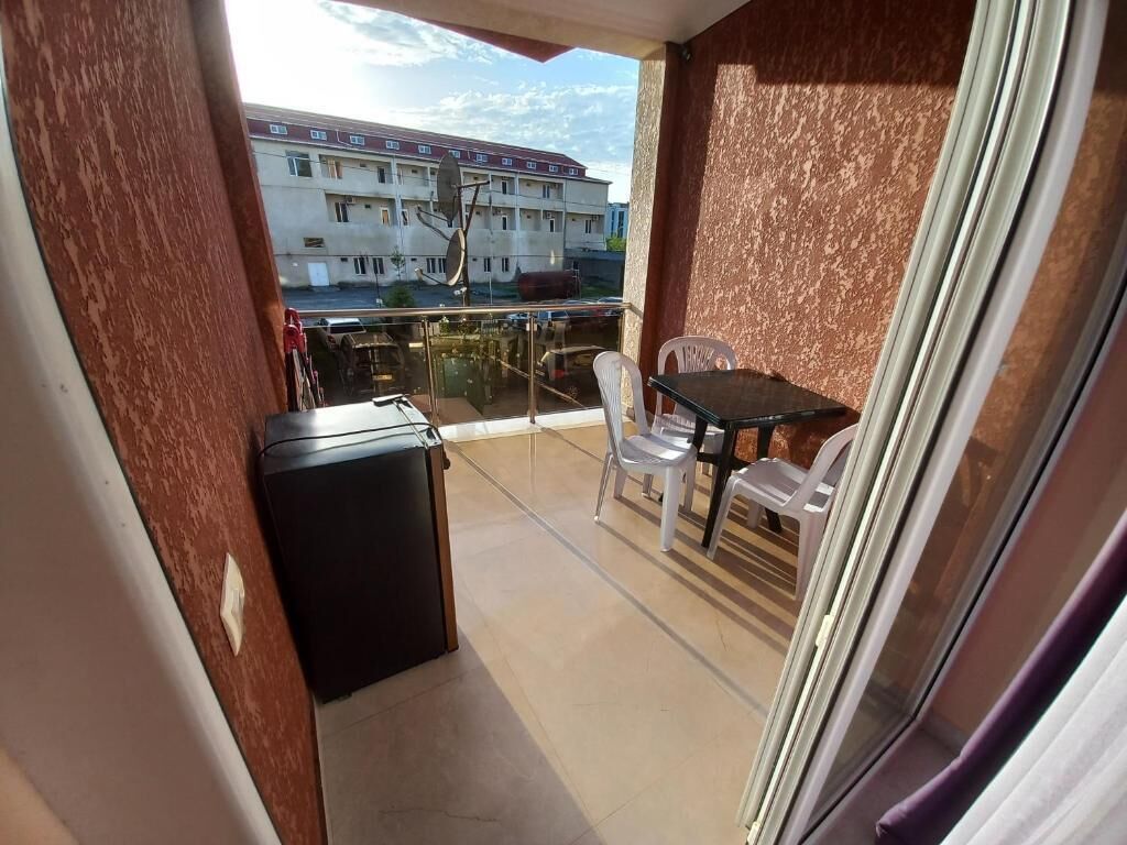 A balcony with a table and chairs, a small refrigerator, and a view of buildings in the background.