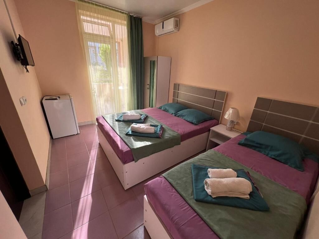 Una habitación de hotel con dos camas, una mesita, un armario y un ventanal con cortinas.